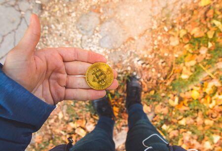 Hand holding a golden bitcoin, blurred background of legs and body. View from above, top-view. Concept of exchange value, money.の写真素材