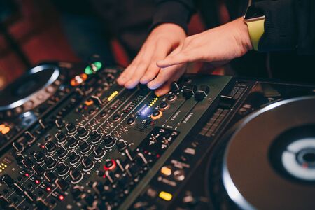 Closeup fingers shot of Dj controling red party dj audio equipment.Turntable top view High quality audio monitors for disc jockey in night club .Pro audio equipment on stage in nightclub.の写真素材