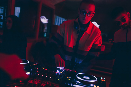 Chisinau, Moldova 11.10.2019. Rave techno DJ plays concert set with CD player turn table & Pioneer sound mixer surrounded by dancing people crowd minimal tracks party mixのeditorial素材