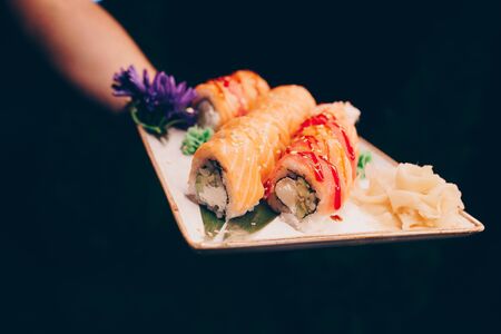 Close-up Hand Waiter holding Set Delicious fresh Sushi slate plate, Japanese raw fish   in traditional restaurant. Philadelphia flesh Rolls served on plate in sushi bar. Copy Space Japan menu serviceの写真素材