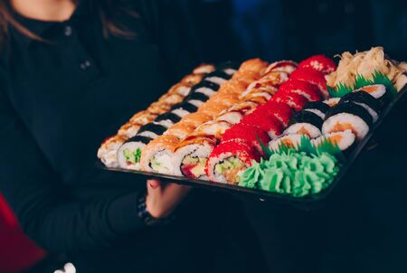 Close-up Hand Waiter holding Set Delicious fresh Sushi slate plate, Japanese raw fish   in traditional restaurant. Philadelphia flesh Rolls served on plate in sushi bar.  Japan food menu serviceの写真素材