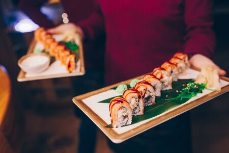 Close-up Hand Waiter holding Set Delicious fresh Sushi slate plate Sushi Rolls Warm Sake Unagi, Japanese raw fish in traditional restaurant. Philadelphia flesh served on plate in luxury sushi bar.  の写真素材