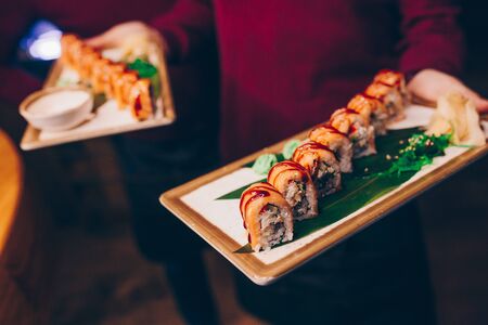 Close-up Hand Waiter holding Set Delicious fresh Sushi slate plate Sushi Rolls Warm Sake Unagi, Japanese raw fish in traditional restaurant. Philadelphia flesh served on plate in luxury sushi bar.  の写真素材