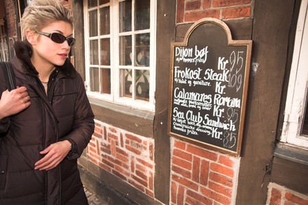 pretty woman outdoor in an old village in denmark looking at a restaurant menu card outside the buildingの写真素材
