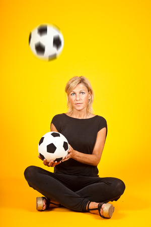 Woman juggling with a soccer ball . In studio with yellow backgroundの写真素材