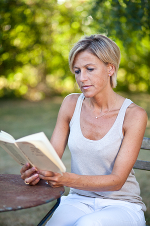 Cute woman reading a book outdoor sitting on a garden chairの写真素材