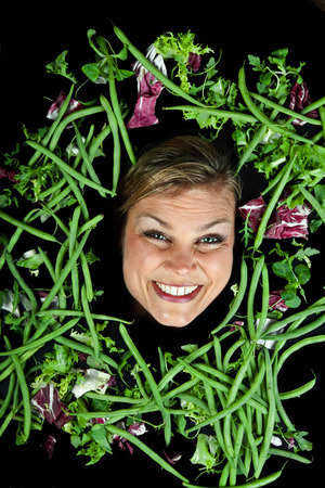 Funny portrait of cute blond girl  with vegetables shot in studio with vegetables aroound the head