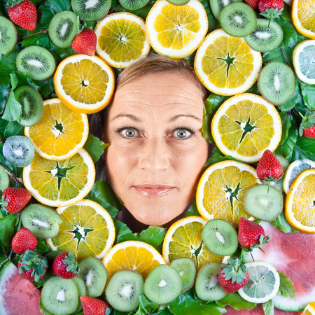 Many fruits stacked together around the head of a cute blond womanの写真素材