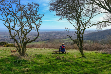 Rear View of a lady sitting contempating on a bench in the South Downs National Park.  Admiring the view and framed by trees.の写真素材