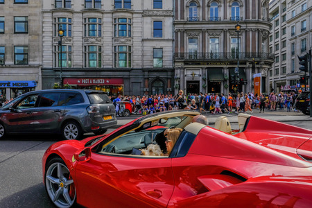 London, UK - April 22, 2018: Couple in an open top red Ferarri car on the road near Trafalgar...