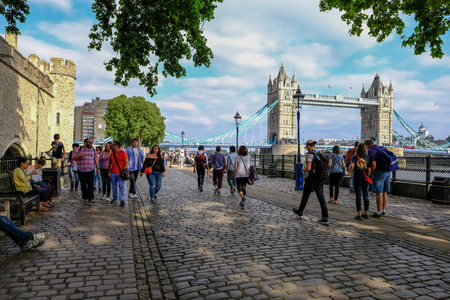 Tower, London, UK - June 8, 2018: Cobbed stones and people strolling beside the Tower of London with Tower Bridge in the background.  Taken on a sunny summer afternoon.のeditorial素材