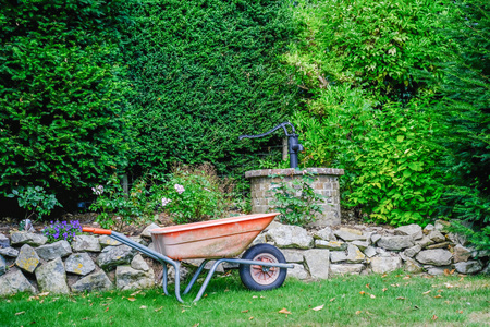 Wheelbarrow in front of a brick well with a black pump.  Taken in an english country garden.の写真素材