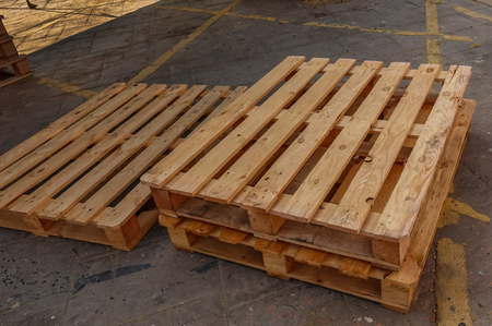 Three wooden pallets stacked on the floor which has yellow markings.