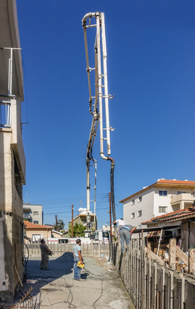 Limassol, Cyprus - April 3, 2018: Delivery of concrete to make a shutter prepared wall.  Long telescopic arm reaching high into the sky to pump cement a long way from the mixer truck.のeditorial素材