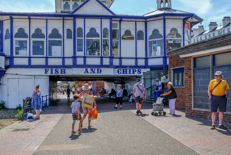 Eastbourne, Sussex, UK - August 1, 2018:  Fish and chips restaurant at the beginning of the pier.  People strolling on the promenade which goes underneath the pier.のeditorial素材
