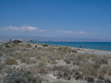 Landscape view of Lady's Mile looking towards the industrial port of Limassol. A wild natural coastal shot with two people walking along the beach.の写真素材