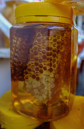 Closeup view of  golden honey with honeycomb in a plastic jar.の写真素材
