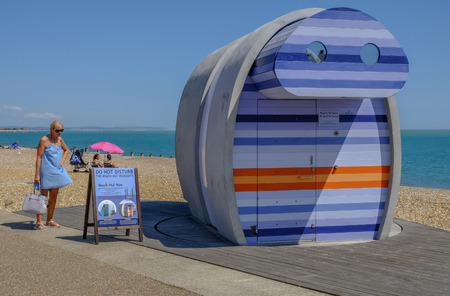Eastbourne, Sussex, UK - August 1, 2018: Lady in blue sun dress reading information about the rentable stripy beach hut called spyglass,  on the beach in Eastbourne.のeditorial素材