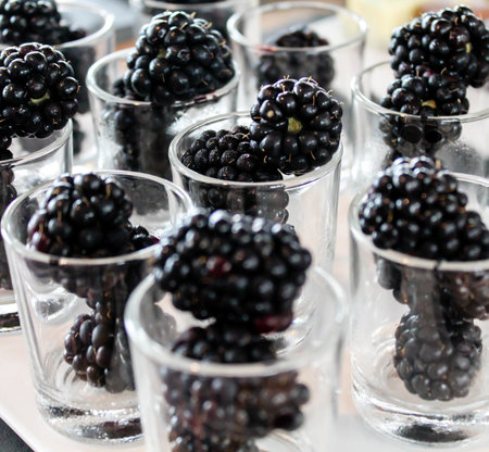 A close-up view of several small glass cups filled with fresh blackberries. The blackberries are...