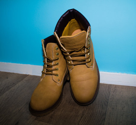 A pair of yellow work boots with brown laces, placed against a light blue wall. The boots are made of leather and have a sturdy sole, suitable for outdoor activities.の写真素材