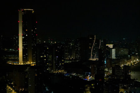 A nighttime cityscape featuring illuminated skyscrapers and buildings along a waterfront. The scene captures the vibrant lights of the city against a dark sky, showcasing modern architecture.の写真素材