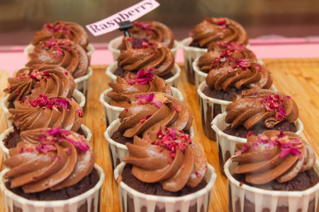 A row of chocolate cupcakes topped with chocolate frosting and sprinkled with dried rose petals....
