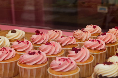 A display of cupcakes with pink and white frosting, topped with crushed red berries. The cupcakes...