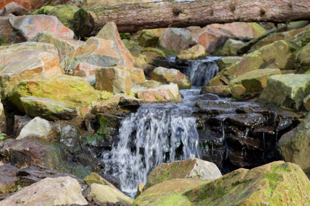 A serene waterfall cascading over rocks in a natural setting, surrounded by moss and greenery. A fallen log rests across the scene, adding to the tranquil atmosphere.の写真素材