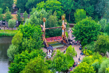Netherlands, Biddinghuizen - July 15, 2014 - Aerial view of a theme park ride resembling a Viking ship, surrounded by lush greenery and a water body. Visitors are seen enjoying the ride and walking nearby.の写真素材