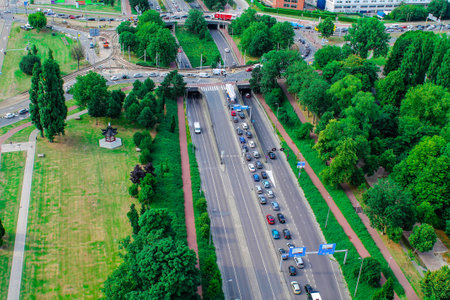 Aerial view of a busy urban highway with traffic, surrounded by greenery and trees. There are vehicles moving in both directions, and a roundabout visible in the background. The scene captures a blend of nature and city life.の写真素材