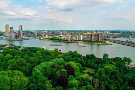 Aerial view of a river winding through a city with modern buildings and lush green parks along the banks. Boats are seen on the water, and the skyline features a mix of architecture under a partly cloudy sky.の写真素材