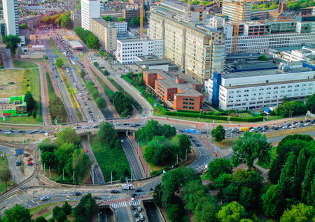 Aerial view of a busy urban intersection with multiple roads, greenery, and buildings. Traffic is visible on the roads, showcasing the hustle of city life.の写真素材