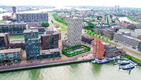 Aerial view of a modern urban landscape featuring a distinctive tower surrounded by residential and commercial buildings, with a river and boats in the foreground.の写真素材