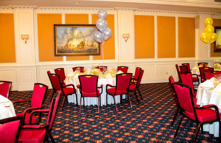 Elegant banquet hall with red chairs, round tables, and festive balloons.の写真素材