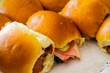 A close-up view of several freshly made sandwiches with soft, golden-brown buns. Some sandwiches are filled with layers of deli meats, lettuce, and pickles, showcasing a delicious assortment of ingredients.の写真素材