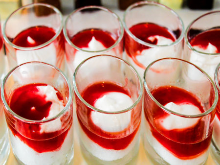 A close-up view of dessert cups filled with layers of cream and red fruit sauce, arranged neatly in a row. The cups feature a creamy white base topped with a vibrant red sauce, creating an appealing visual contrast.の写真素材