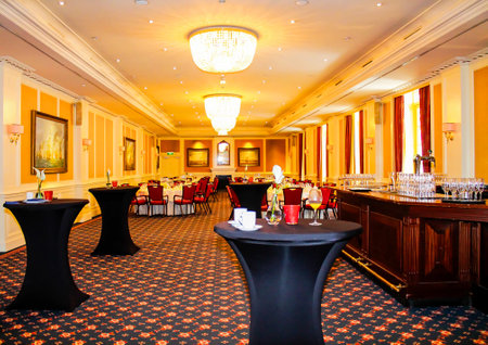 Elegant banquet hall with round tables and black tablecloths, featuring a bar area and decorative chandeliers. The room is well-lit with warm colors and classic decor.の写真素材