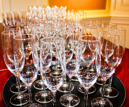 A collection of sparkling clean glassware arranged neatly on a tray, featuring various types of glasses including champagne flutes and wine glasses, set against a softly lit background.の写真素材
