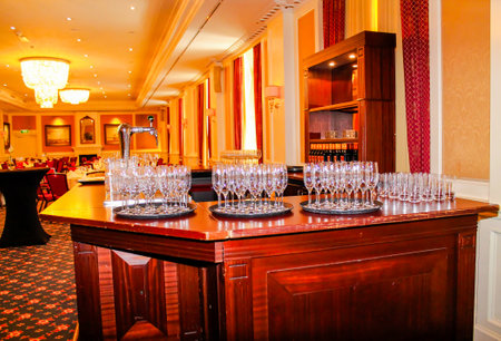 A beautifully arranged bar area with multiple trays of sparkling glasses, set in an elegant banquet hall. The warm lighting and luxurious decor create a sophisticated atmosphere.の写真素材