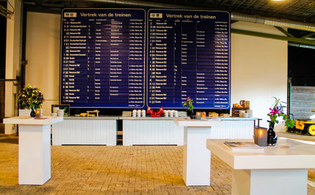 Indoor event setup with tables and a large train departure board.の写真素材