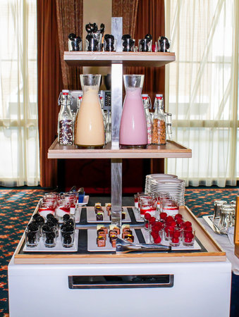 A beautifully arranged dessert table featuring two glass pitchers filled with beverages, assorted small desserts in glasses, and colorful treats on a tiered display. The setting is elegant with natural light streaming in.の写真素材