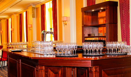 A beautifully arranged bar area featuring numerous sparkling glasses on a polished wooden counter, with elegant decor and soft lighting in the background.の写真素材