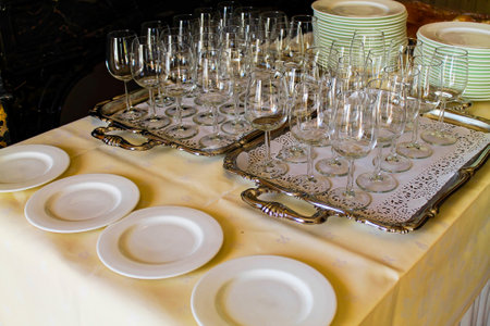 A beautifully arranged table setting featuring multiple trays of clear wine glasses and white plates. The elegant display is perfect for a formal dining occasion or event.の写真素材