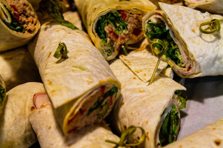 A close-up view of rolled wraps filled with greens, meats, and spreads, arranged on a surface. The wraps are neatly rolled and garnished with green herbs.の写真素材