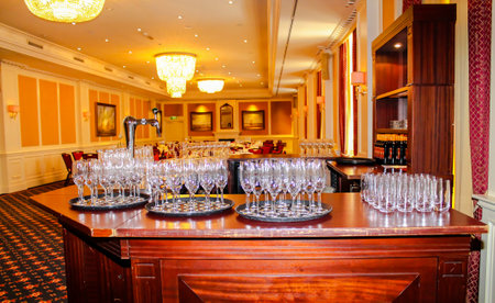A beautifully arranged bar area in a banquet hall, featuring multiple trays of sparkling clean wine glasses. The elegant decor includes chandeliers and soft lighting, creating a sophisticated atmosphere.の写真素材