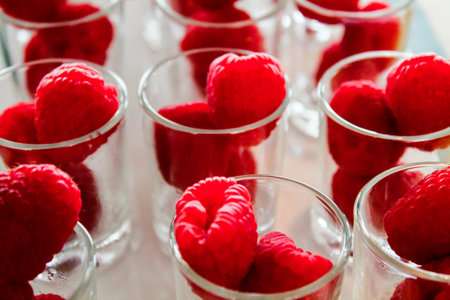 Close-up of fresh raspberries placed in small glass cups, showcasing their vibrant red color and texture. Ideal for food photography or culinary presentations.の写真素材