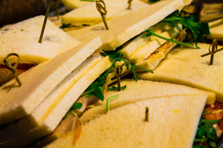 A close-up of neatly arranged sandwiches with white bread, garnished with green herbs and secured with toothpicks. The sandwiches appear fresh and ready to serve, showcasing layers of filling.の写真素材
