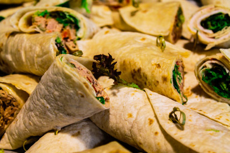 A close-up view of rolled tortillas filled with various ingredients, including greens and meat, arranged neatly on a platter.の写真素材