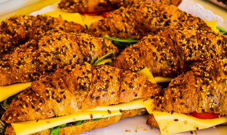 A close-up view of several sesame-seed topped croissants filled with cheese, lettuce, and tomato, arranged neatly on a platter.の写真素材