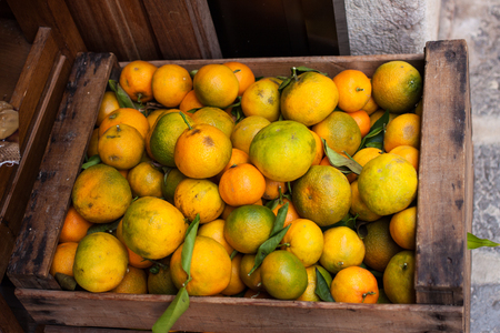 Wooden basket of greenish mandarin oranges (tangerins) with green leaves for saleの写真素材